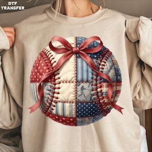 Peut inclure: Un sweat-shirt beige avec un motif de baseball. Le ballon est fait de patchwork rouge, blanc et bleu, et est orné d'un ruban rouge. Le texte "DTF TRANSFER" est dans le coin supérieur gauche.