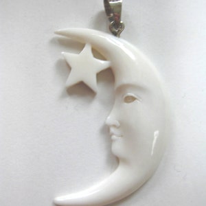 May include: White bone pendant carved in the shape of a crescent moon with a star inside. The moon has a face carved into it. The pendant has a silver bail.