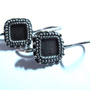 May include: A pair of silver earrings with a square design. The earrings have a beaded border and a smooth, silver centre.
