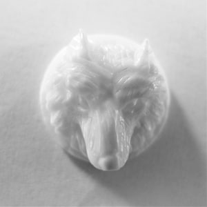 May include: White ceramic wolf head sculpture. The wolf's head is facing forward with its mouth closed. The sculpture is detailed with fur and facial features.