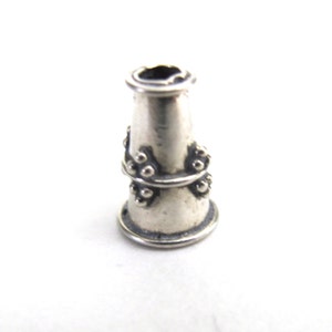 Puede incluir: Cuente de plata de forma cónica con una banda decorativa de pequeñas cuentas alrededor del centro.