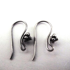 May include: A pair of silver-toned earrings. Each earring features a curved hook design with a small cluster of round beads at the bottom. The earrings are displayed against a white background.