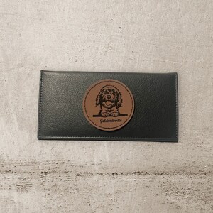 May include: Black leather wallet with a brown leather patch featuring a doodle of a dog with the text "Goldendoodle" underneath.