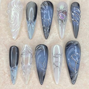 Puede incluir: Una colección de diez diseños de uñas largas y puntiagudas. Las uñas presentan una variedad de colores, incluyendo blanco, gris y azul, con intrincados diseños plateados. El texto "Nail Art" está en la parte superior y el texto "Thank you for your order. I hope you like it." en la parte inferior.