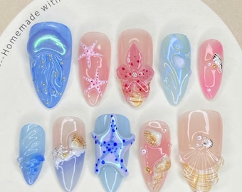 Puede incluir: Una colección de diez puntas de uñas con varios diseños temáticos del océano. Las puntas presentan bases azules, rosas y transparentes con diseños de estrellas de mar, conchas marinas y medusas. El texto "Nail Tip" es visible en la parte inferior.