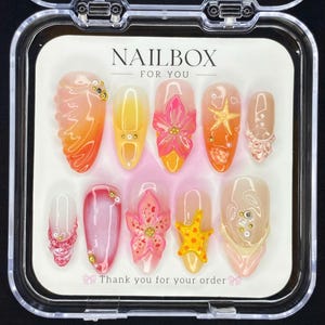 May include: A collection of ten artificial nails in a clear case. The nails showcase diverse designs, including floral patterns and starfish, in shades of orange, pink, and yellow. The text "NAILBOX FOR YOU" and "Thank you for your order" are displayed on the packaging.