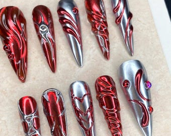 Puede incluir: Un conjunto de diez uñas postizas largas y puntiagudas. Las uñas alternan entre plata metálica y rojo intenso, con diseños intrincados. El texto "Nail Art" es visible en la parte superior.