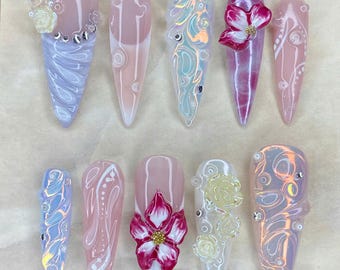 Può includere: Dieci unghie finte a forma di mandorla, ognuna con design unici. Presentano decorazioni floreali, accenti iridescenti e motivi intricati. Il testo "Nail Art" e il messaggio "Thank you for your order. I hope you like it." sono inclusi.