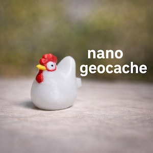 May include: A white, hen-shaped nano geocache container with a red comb and wattle, and a yellow beak. The text "nano geocache" is displayed in white on the right side of the image. The hen is sitting on a light-colored surface.