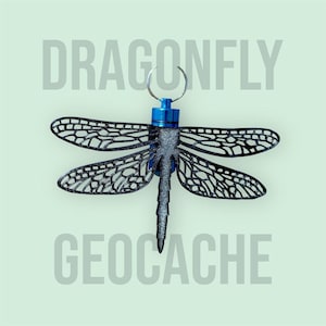 May include: A dragonfly geocache with a black, openwork design. The wings and body are detailed with a glittery finish. The top is blue with a silver keyring. The word "DRAGONFLY" is above the dragonfly and "GEOCACHE" is below.