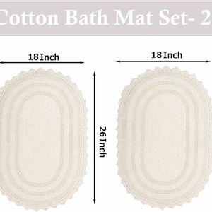 Könnte beinhalten: Zwei cremefarbene Baumwoll-Badematten, jeweils 45,7 cm breit und 66 cm lang. Die ovalen Matten haben einen gewellten Rand und ein strukturiertes Design. Der Text "Cotton Bath Mat Set- 2" steht oben.