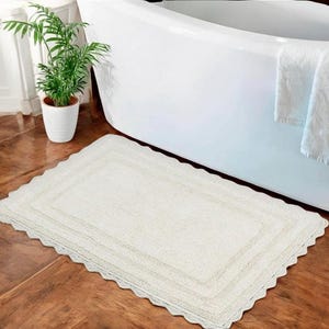 Könnte beinhalten: Eine weiße Badematte mit einem gewellten Rand und einem gehäkelten Saum. Die Matte besteht aus einem weichen, saugfähigen Material und ist perfekt für die Verwendung im Badezimmer.