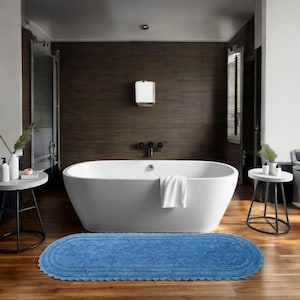 Könnte beinhalten: Ein modernes Badezimmer mit einer weißen ovalen Badewanne, einer blauen ovalen Badematte und zwei kleinen Beistelltischen. Die Wände sind dunkelbraun und der Boden ist aus Hartholz. Ein weißes Handtuch ist über der Wanne drapiert.