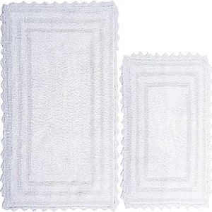 May include: Two white rectangular bath mats with a scalloped edge. The larger mat has a rectangular border and vertical lines in the center. The smaller mat has a similar design. Both mats are made of a soft, absorbent material.