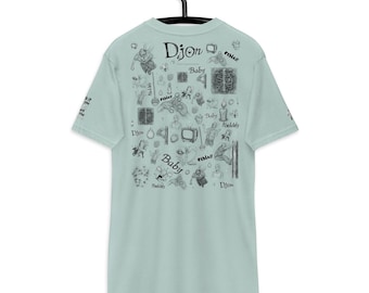 Può includere: Una maglietta azzurra con un design grafico nero. Il design include la parola "Dijon" e la parola "Baby" insieme a varie illustrazioni. La maglietta è appesa a una gruccia nera.