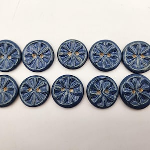 May include: Ten navy blue ceramic buttons with a citrus fruit design. Each button has a two-hole design and a textured surface. The buttons are arranged in two rows on a white surface.