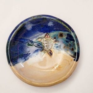 May include: A small ceramic dish with a blue and white glaze. A 3D sea turtle is in the center of the dish.