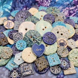 May include: A collection of handmade ceramic buttons in shades of blue and white. The buttons feature various designs, including swirls, geometric patterns, and floral motifs.