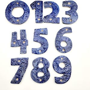 May include: Set of ten blue ceramic house numbers with a decorative swirl pattern. The numbers are 0 through 9.