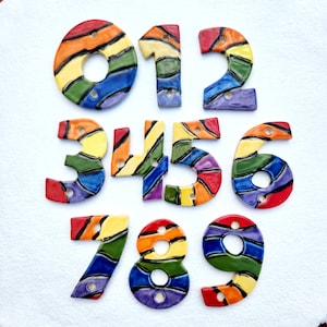 May include: Set of ten ceramic house numbers, each painted with a rainbow stripe pattern. The numbers are 0 through 9.