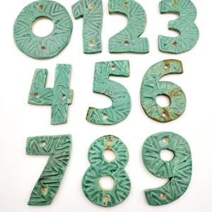 May include: Set of ten ceramic house numbers in a teal green color with a textured pattern. The numbers are 0 through 9.