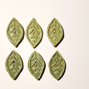 Puede incluir: Seis botones de cerámica verde en forma de hoja con un patrón de nervaduras en relieve y dos agujeros cada uno.