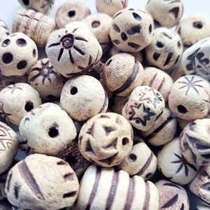 May include: A collection of beige ceramic beads with various brown etched designs. The beads are all different shapes and sizes, and some have holes in the centre.