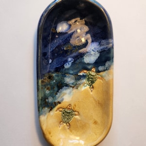 May include: A ceramic dish with a blue and yellow glaze. The dish has two sea turtles painted on it.