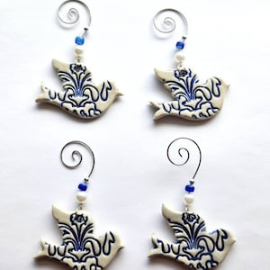 May include: Four ceramic dove ornaments with a white base and intricate blue floral designs. Each dove has a silver wire loop for hanging, adorned with blue and white beads. The ornaments are ideal for home decor.
