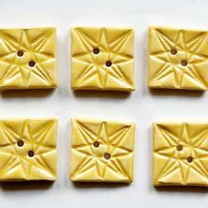 May include: Six yellow ceramic buttons with a starburst design and two holes each.