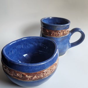 May include: A set of two blue ceramic mugs with brown decorative bands. The mugs are handmade and have a rustic look.
