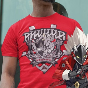 May include: Red t-shirt with a graphic design featuring a cartoon character and the text "PSYCHO" in a stylised font. The character is wearing a crown and holding a weapon. The graphic is surrounded by stars and a shield.
