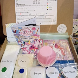 May include: Unicorn-themed cupcake baking kit with ingredients, cupcake cases, sprinkles, and a puzzle book. The kit includes flour, sugar, icing sugar, sprinkles, and toppers. The ingredients are labelled in white circles with red, blue, and green dots.