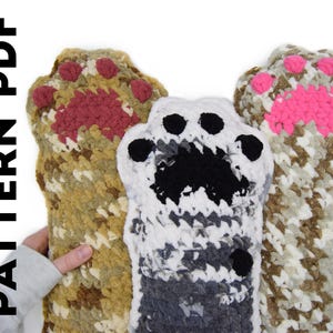 May include: Three crocheted paw-shaped items in shades of brown, white, and gray, each with a different colored paw pad design. The text "PATTERN PDF" is vertically aligned on the left side of the image.