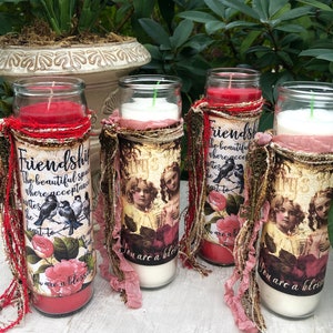 May include: Four decorative candles with red, white, and gold accents. Each candle has a different design and text. The text on the candles reads "Friendship", "The beautiful space where acceptance invites the heart to", "You are a blessing", and "You are a blessing".