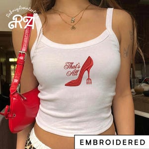May include: White tank top with a red embroidered design of a high heel shoe with a trident heel and the text "That's All". The word "EMBROIDERED" is printed at the bottom of the image.