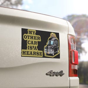 May include: A black and gold car magnet with the text "My other car is a hearse" and a cartoon image of a black hearse with two skeletons on top.