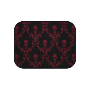 May include: A rectangular mat featuring a black background with a repeating dark red damask pattern. The design incorporates stylized skulls integrated into the ornate, swirling floral motifs across the entire surface of the mat.