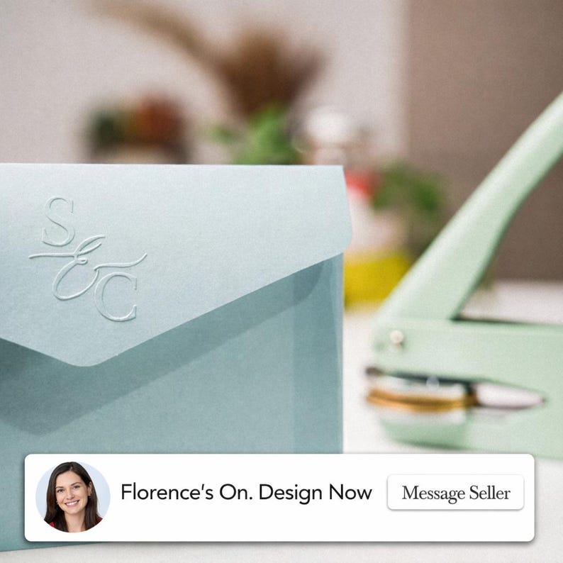May include: A light blue envelope with embossed initials, next to a mint green paper punch. The envelope has a flap closure and the initials "S E C" are visible. The text "Florence's On. Design Now" is displayed at the bottom.