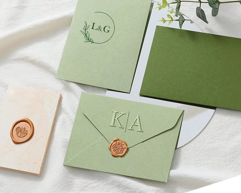 May include: Light green wedding invitation suite with embossed initials and a wax seal. The suite includes envelopes, cards, and a decorative wax seal. The design features a minimalist aesthetic with a focus on elegant typography and a natural color palette.