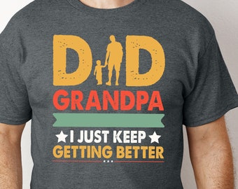 Może przedstawiać: Szary t-shirt z grafiką w stylu vintage, na której widnieje napis "Dad Grandpa I Just Keep Getting Better". Grafika przedstawia sylwetkę ojca i syna trzymających się za ręce.
