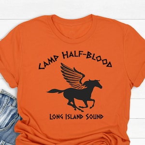 Peut inclure: T-shirt orange avec un logo noir Camp Half-Blood représentant un cheval ailé et le texte "Long Island Sound".