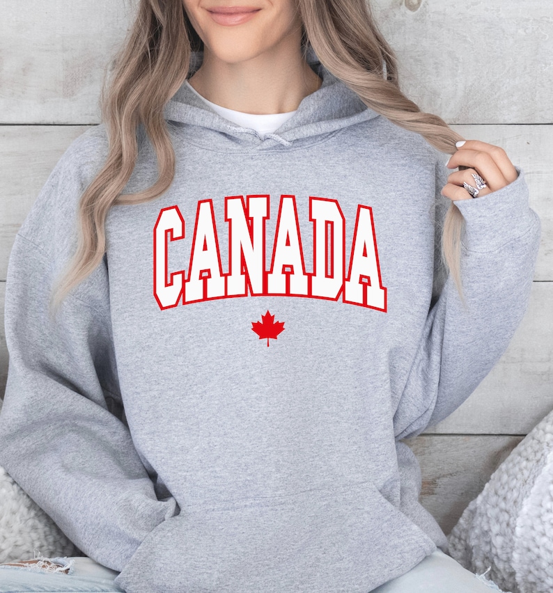 Peut inclure: Sweat-shirt &agrave; capuche gris avec le mot "CANADA" en lettres blanches sur fond rouge et une feuille d'&eacute;rable rouge en dessous.
