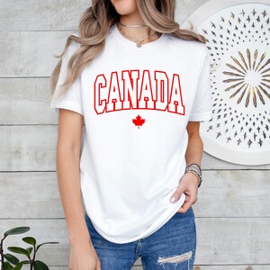 Peut inclure: T-shirt blanc avec le texte rouge "CANADA" et une feuille d'&eacute;rable rouge en dessous.