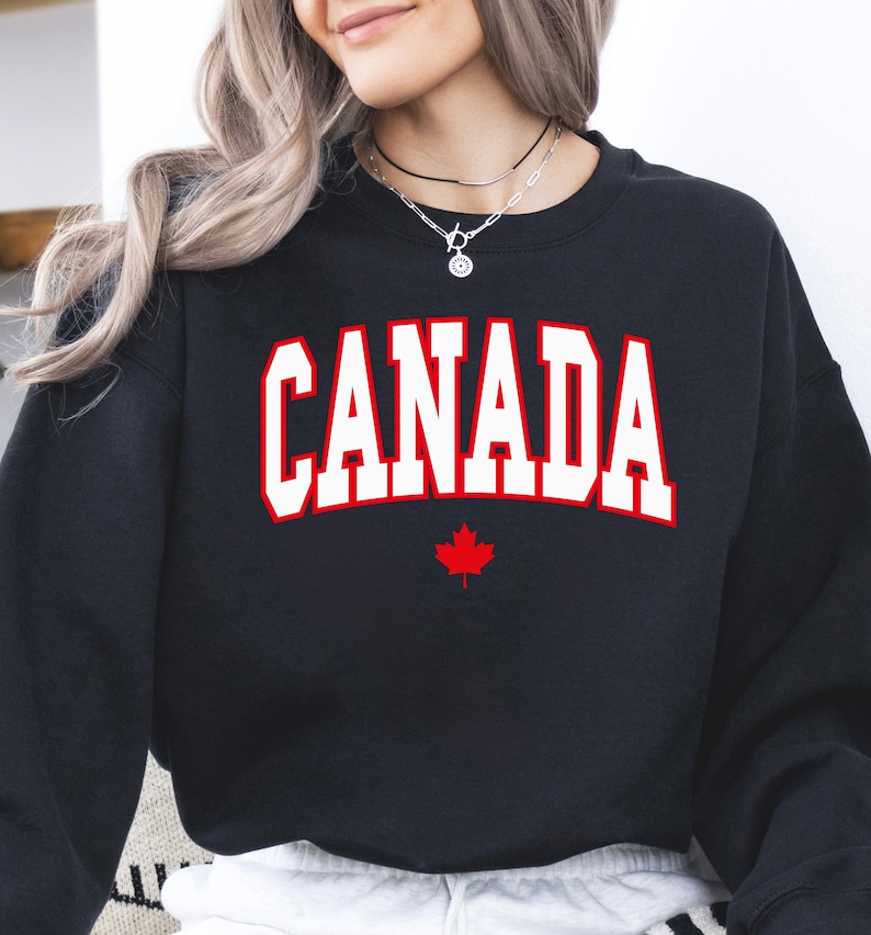 Peut inclure: Sweat-shirt noir avec le texte blanc "CANADA" et une feuille d'&eacute;rable rouge.