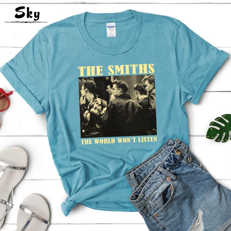 May include: A light blue t-shirt with a black and white image of a band. The band is called "The Smiths" and the text "The World Won't Listen" is printed below the image.