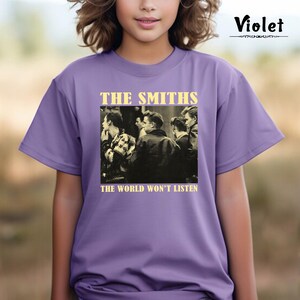 May include: A purple t-shirt with a black and white photo of a band on the front. The band is called "The Smiths" and the text below the photo says "The World Won't Listen."