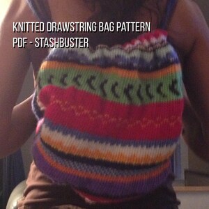 Puede incluir: Un bolso de punto con cordón y un colorido diseño de rayas en rojo, verde, azul, naranja y morado. El bolso tiene un aspecto texturizado y el texto "KNITTED DRAWSTRING BAG PATTERN PDF - STASHBUSTER" es visible.