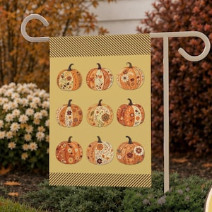 Puede incluir: Una bandera de jardín rectangular con un fondo amarillo mostaza y una cuadrícula de nueve calabazas ilustradas, cada una decorada con complejos patrones florales y de hojas. Los bordes superior e inferior tienen una franja diagonal.