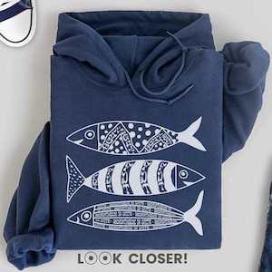 May include: Navy blue hooded sweatshirt with a white design of three stylized fish. The text "LOOK CLOSER!" is printed below the fish. The text "GILDAN" is printed on the left side of the image and "navy" is printed below it. The text "more colors!" is printed in the upper right corner of the image.